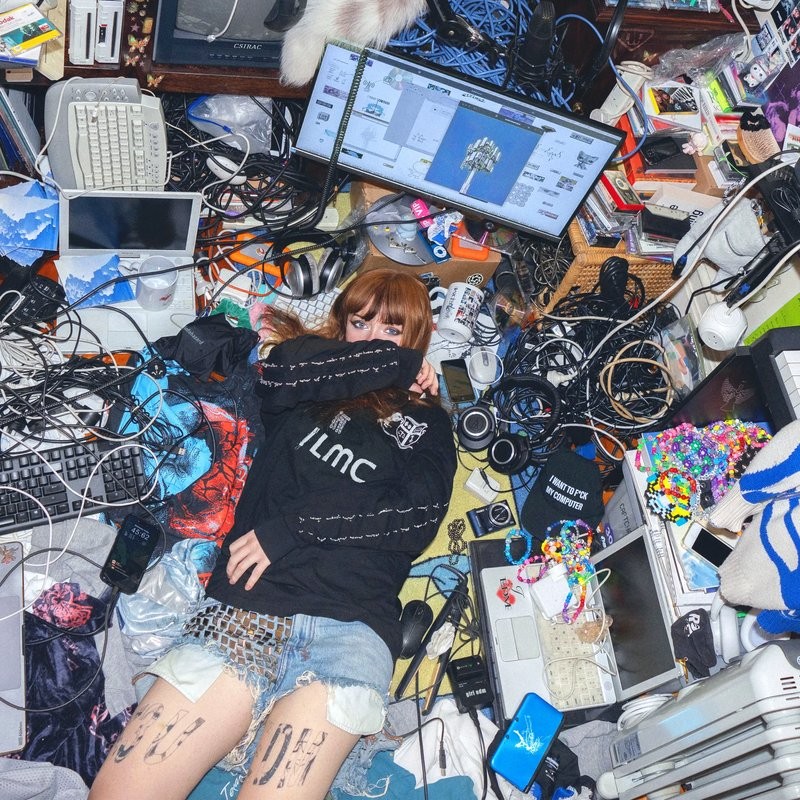 Overhead view of a bedroom studio setup, monitors, cables, and gear scattered around someone lying on the floor
